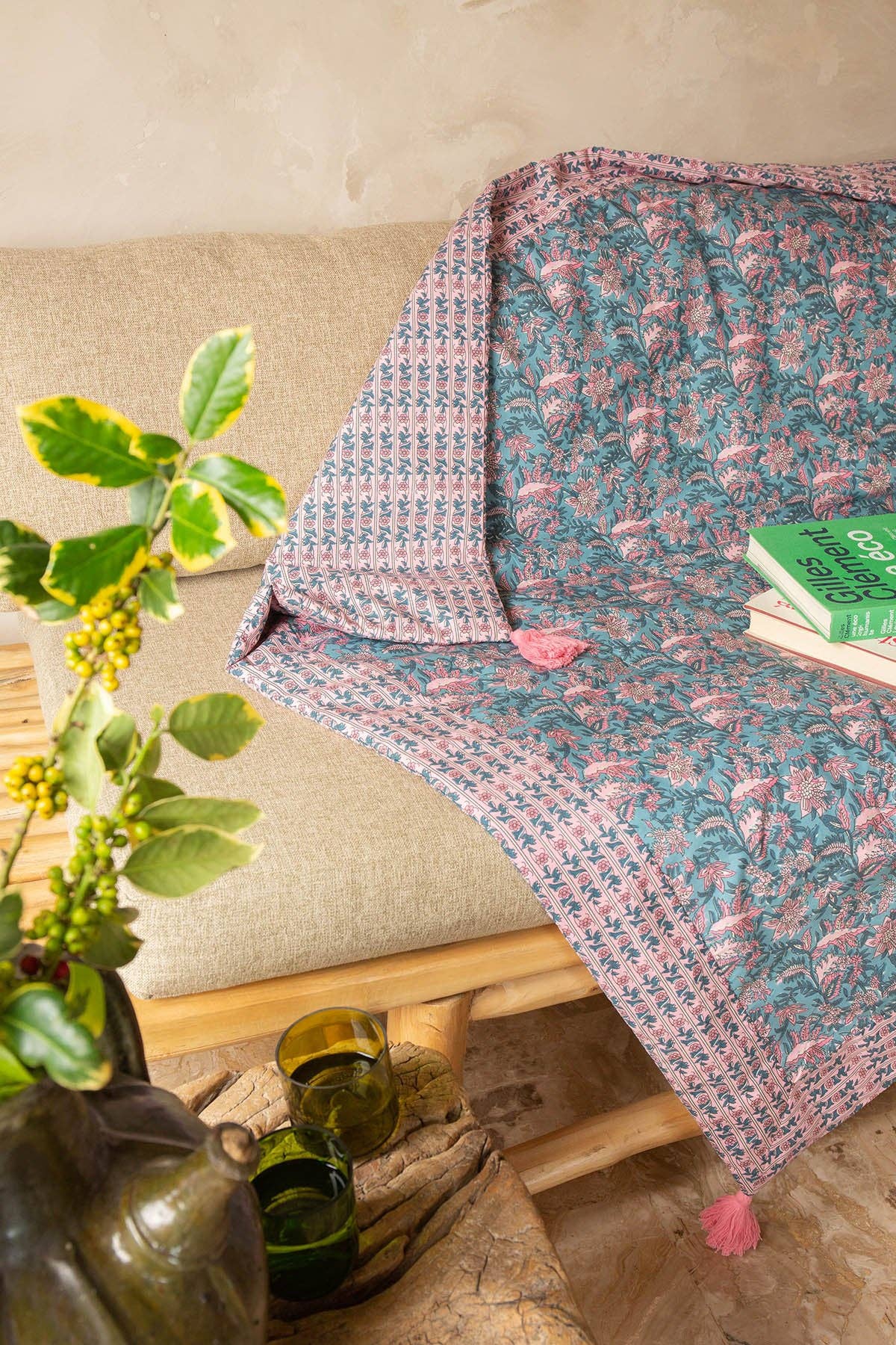 Floral patterned throw blanket draped over a sofa with a plant and books in the foreground.