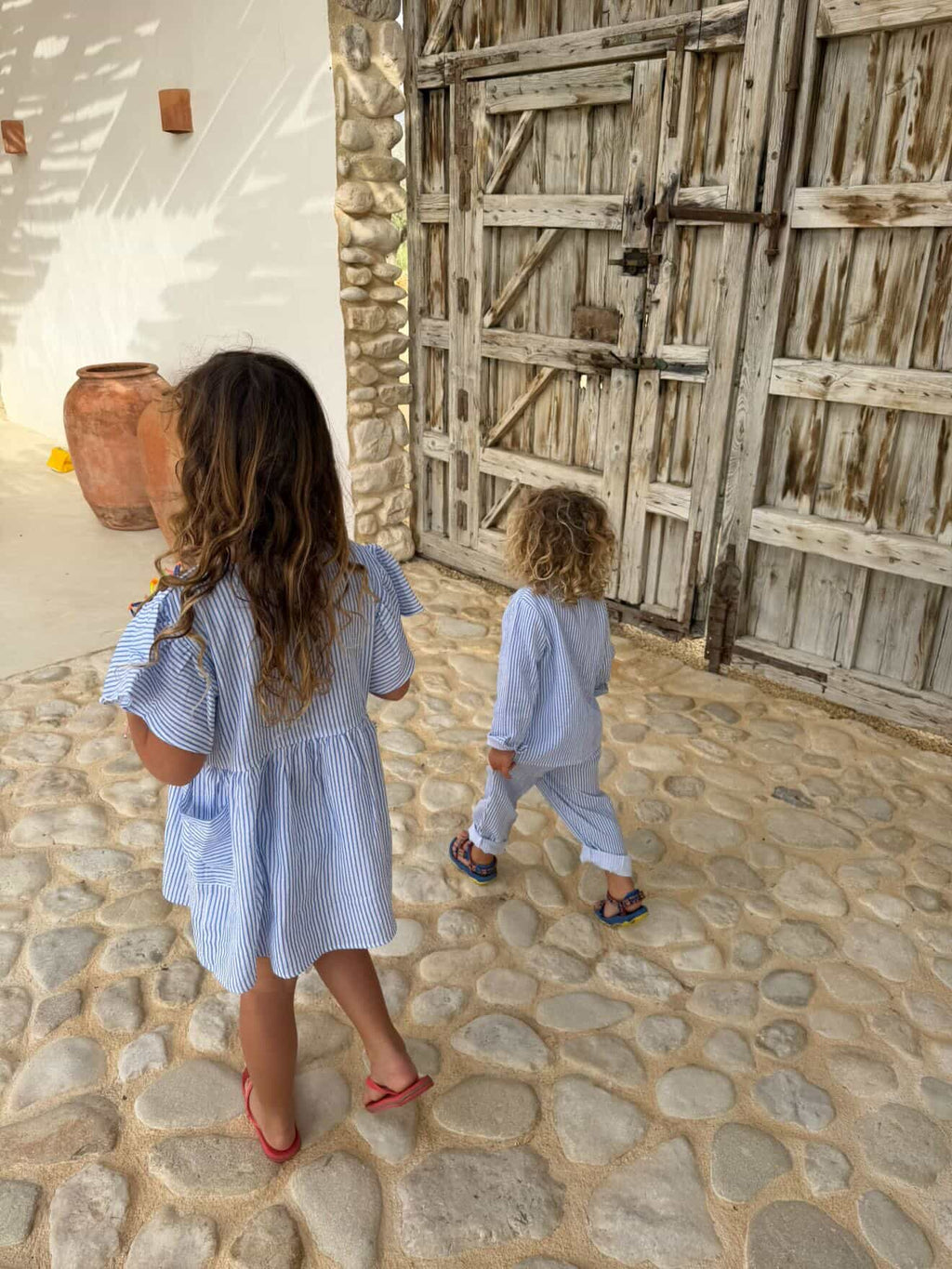 Two children walking on a stone path in front of a rustic wooden door.