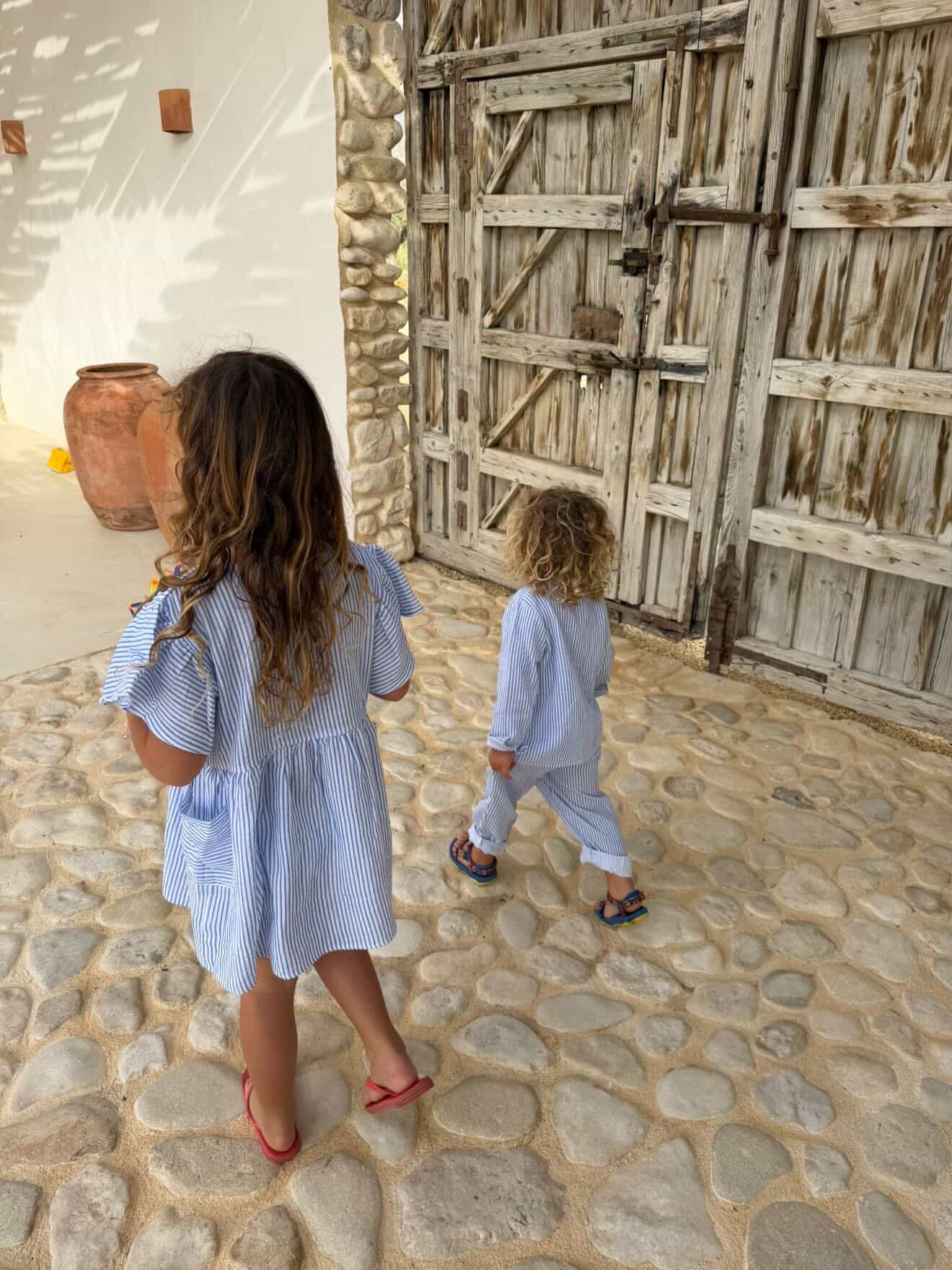 Two children walking on a stone path in front of a rustic wooden door.