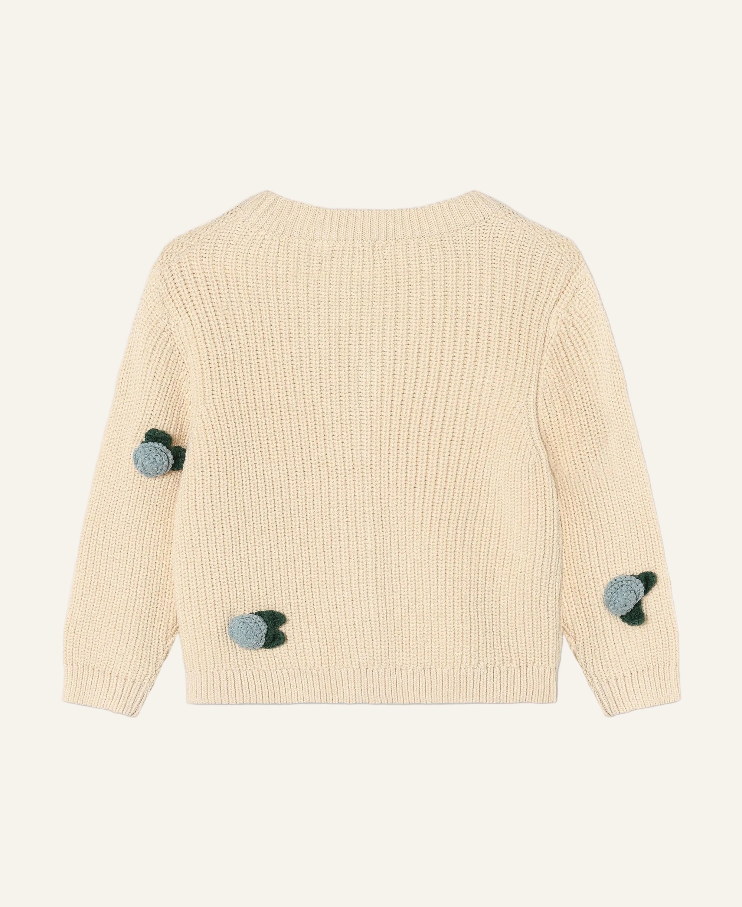 A cream-colored ribbed knit sweater with three small decorative pom-pom embellishments on the sleeves and lower back, shown from the back against a light gray background.