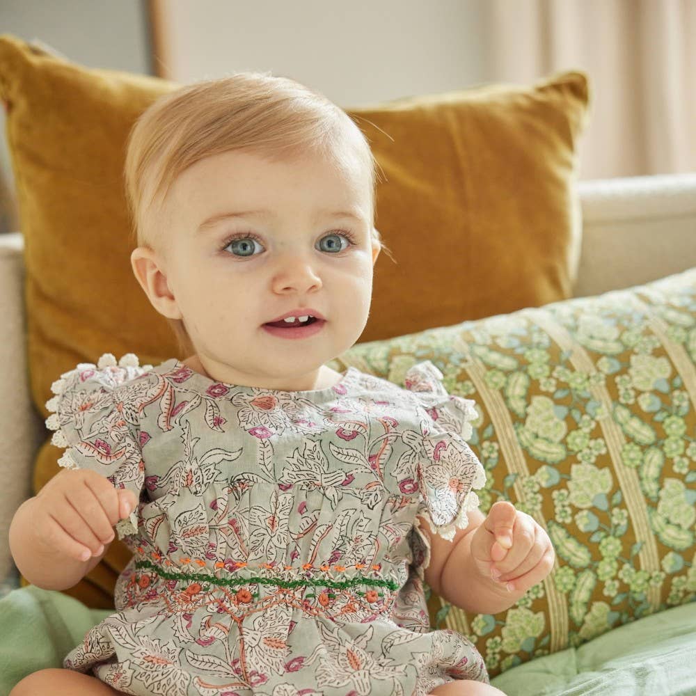 Baby in a floral dress sitting on a couch with patterned cushions