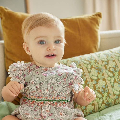 Baby in a floral dress sitting on a couch with patterned cushions