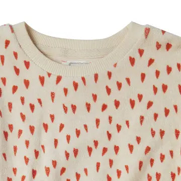 Close-up of a cream-colored knit top with a repeating pattern of small red hearts, showing the ribbed crew neck collar.