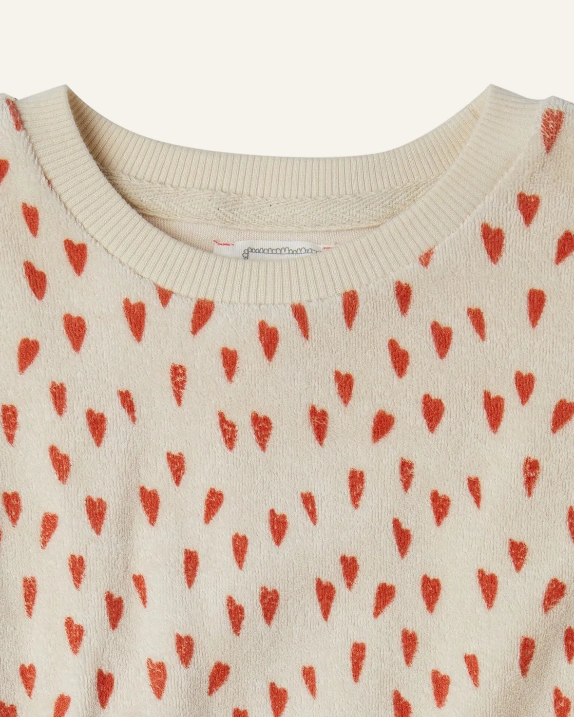 Close-up of a cream-colored knit top with a repeating pattern of small red hearts, showing the ribbed crew neck collar.