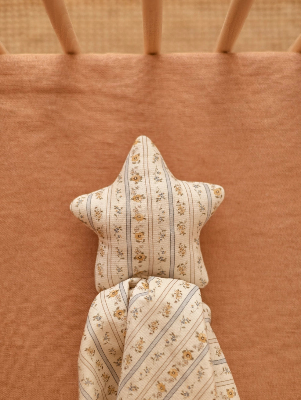 A close-up of a star-shaped baby pillow and matching folded blanket with a cream floral and striped pattern, placed on a warm peach-colored mattress.