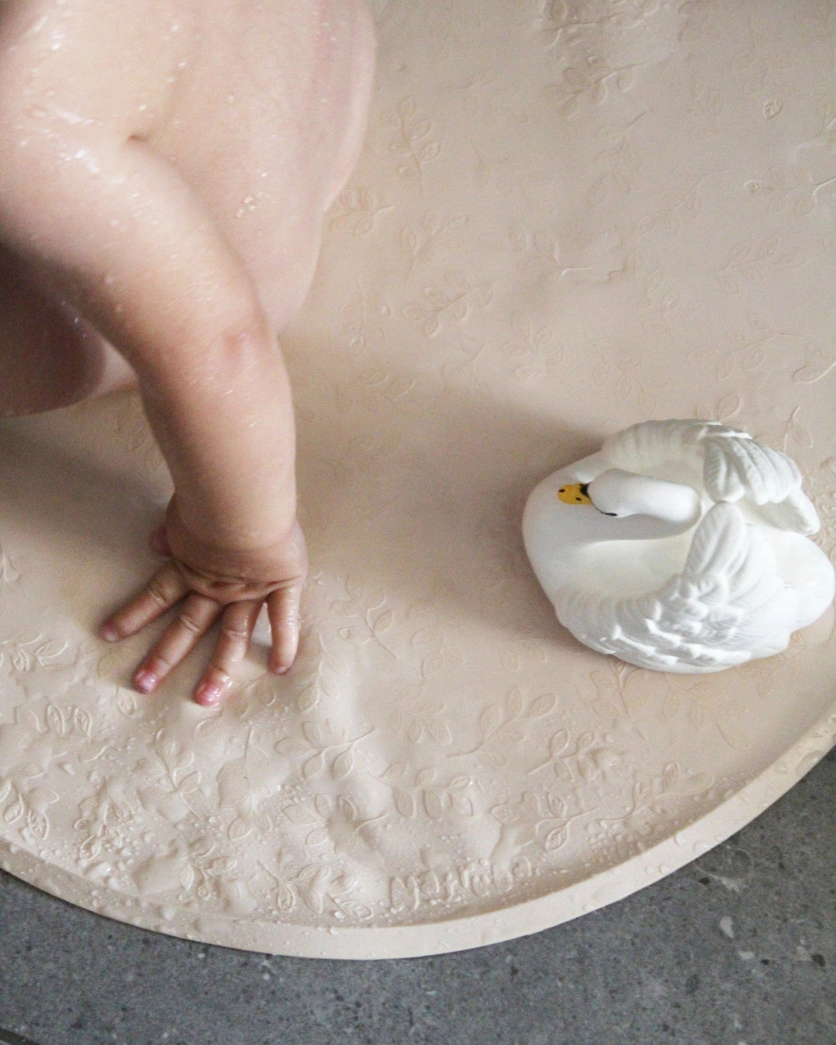 Child's hand reaching towards a white swan toy on a textured surface