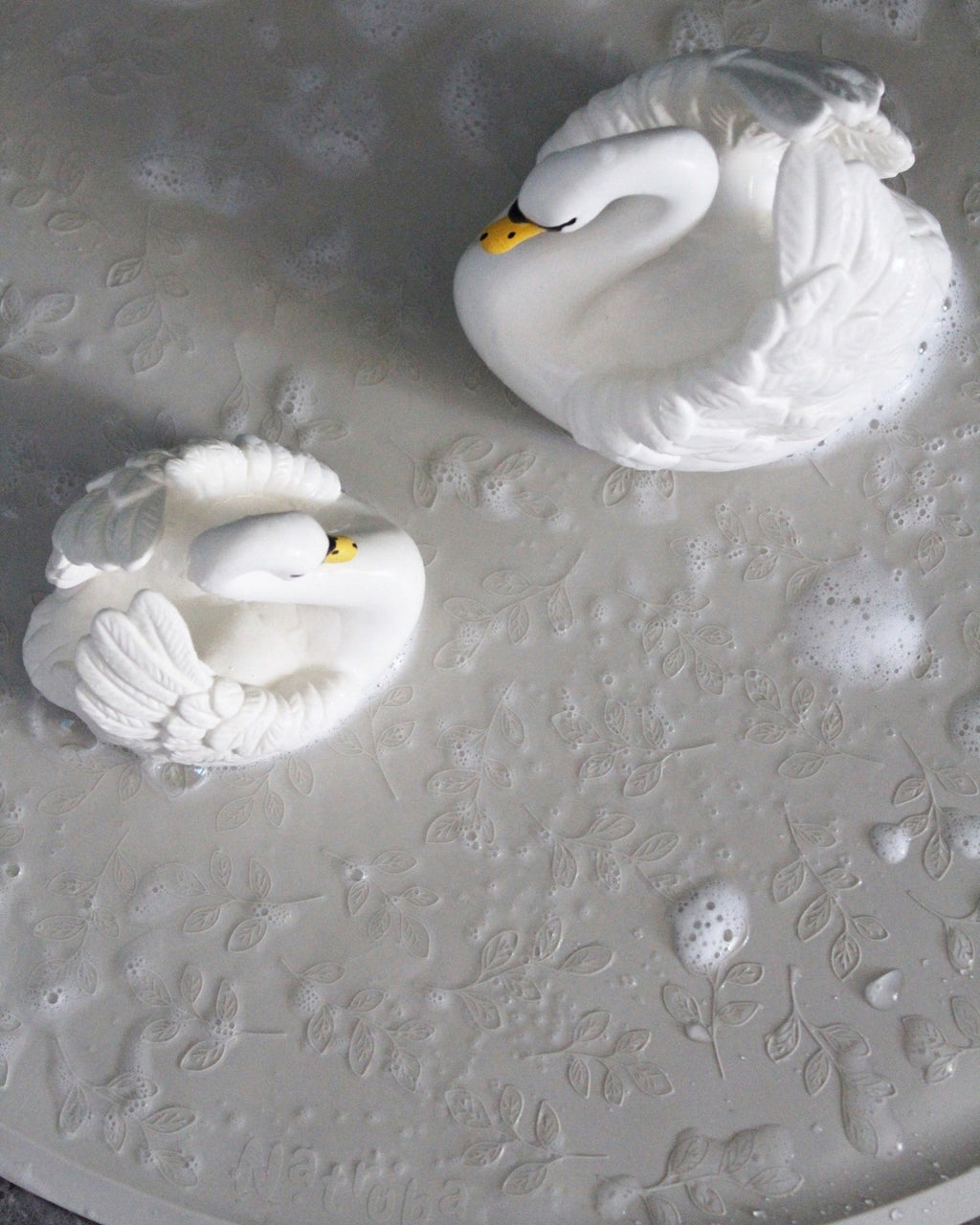 Two white swan figurines on a textured white surface