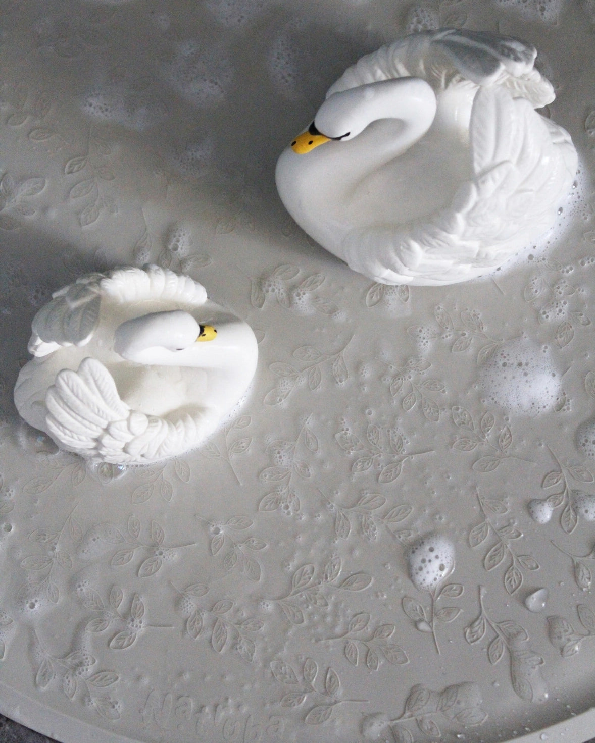 Two white swan figurines on a textured white surface