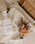 White bottle labeled 'MINGIS' on a textured surface with dried flowers and a woven basket.
