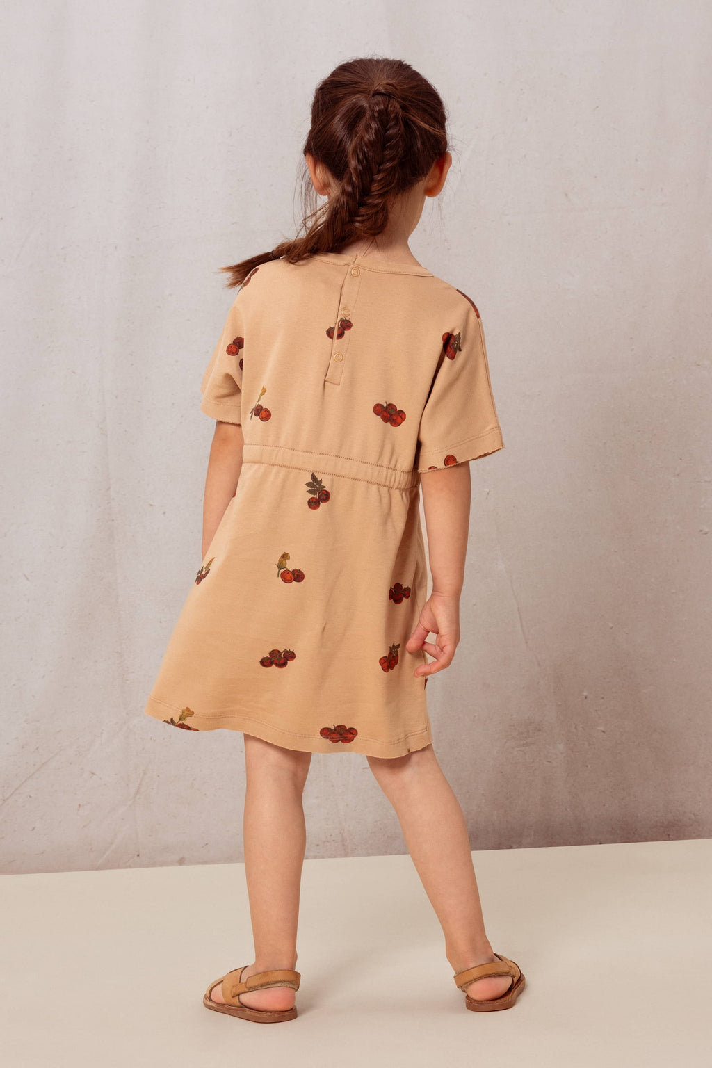 Child wearing a beige dress with cherry patterns against a plain background