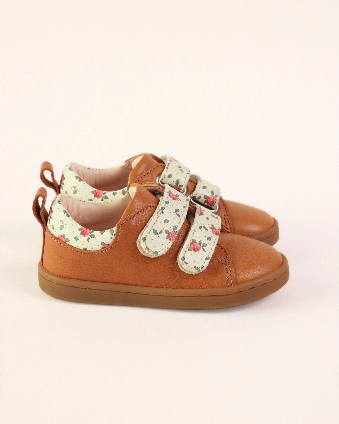 A pair of toddler's brown leather shoes with floral-patterned velcro straps, shown on a light beige background.