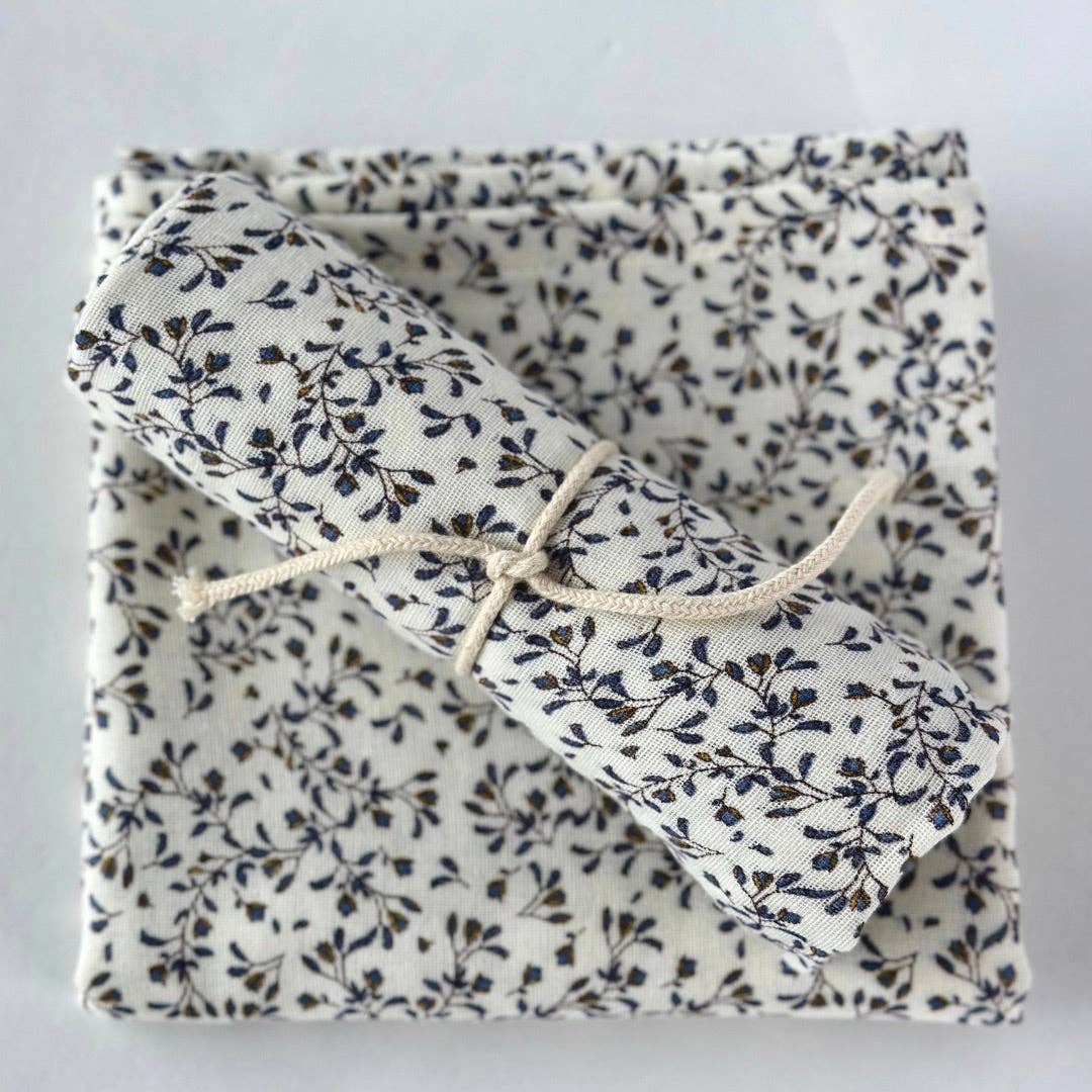 A folded and rolled piece of fabric with a delicate black floral and leaf print on a warm off-white background, tied with a simple beige twine string, presented on a neutral light gray background.
