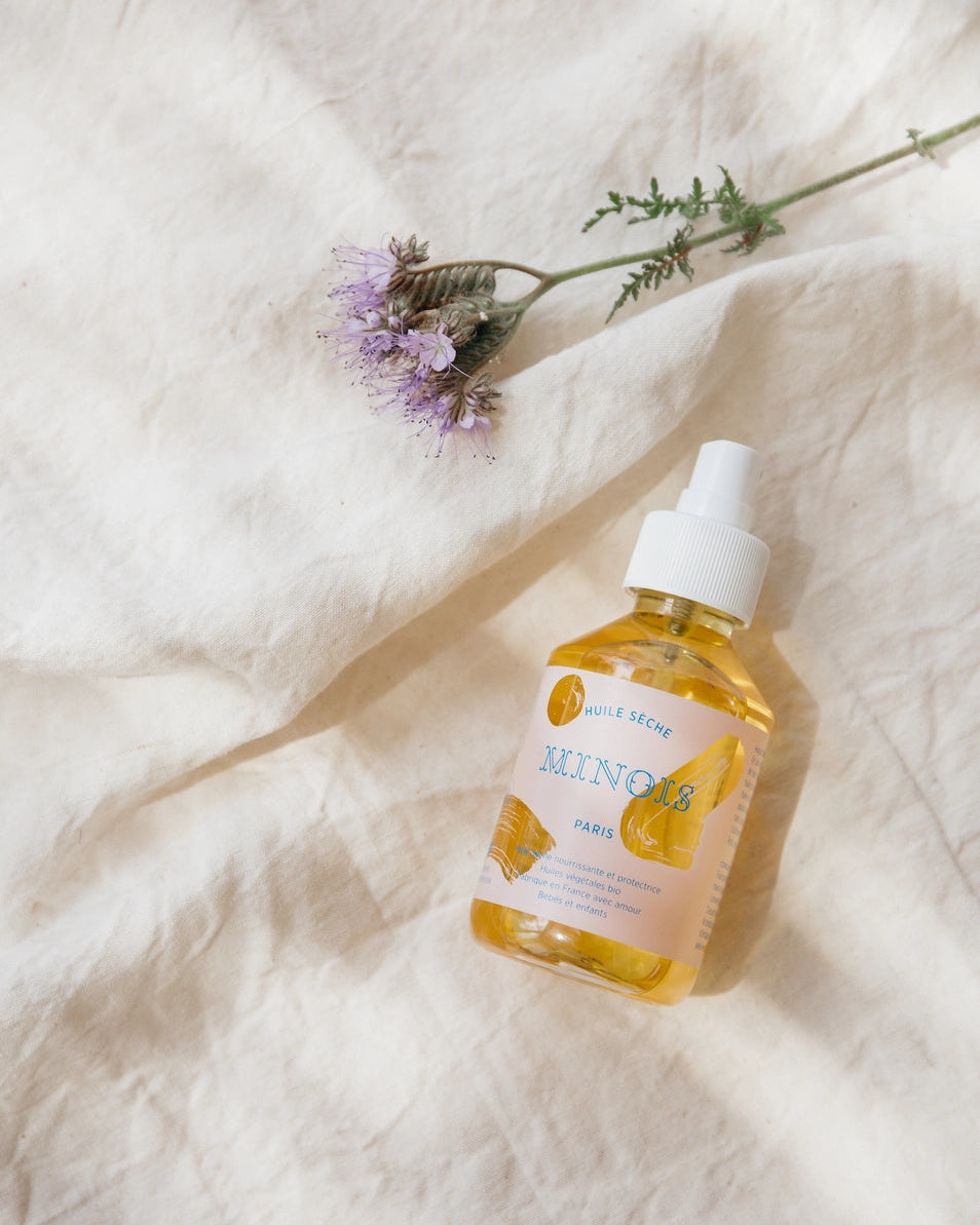 Bottle of Minois dry oil on a textured white surface with a flower.