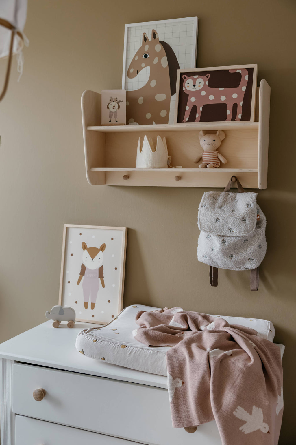 Nursery room with wooden shelf, stuffed animals, and baby items on a beige wall.