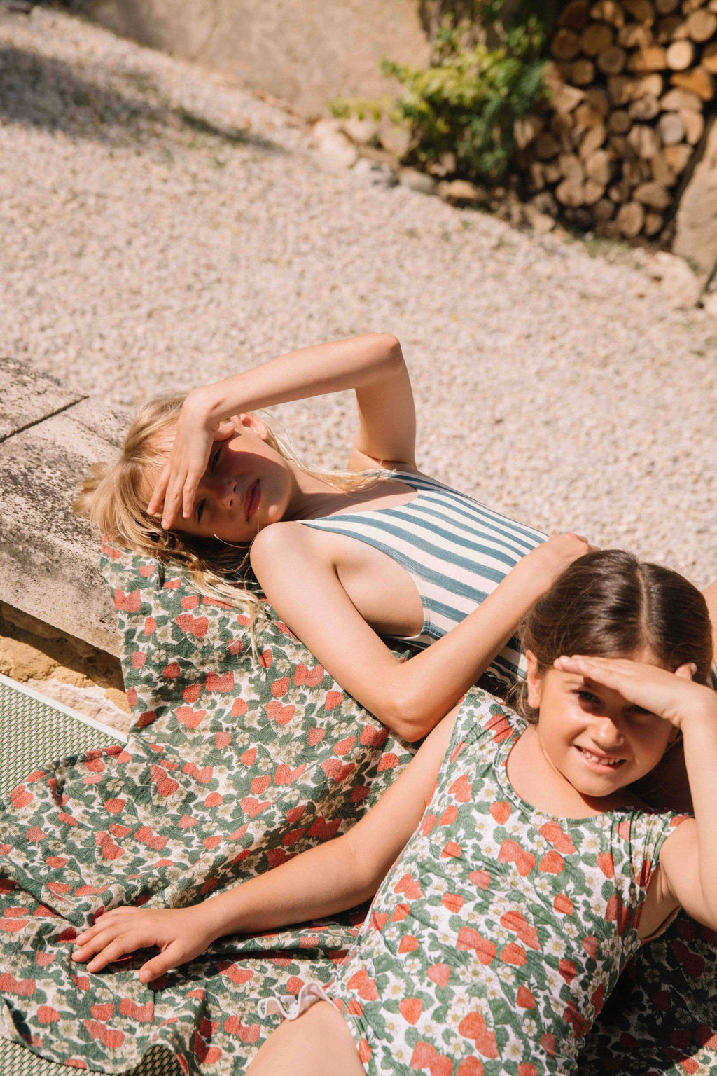Two women in floral dresses lying on a stone surface with a rustic background.