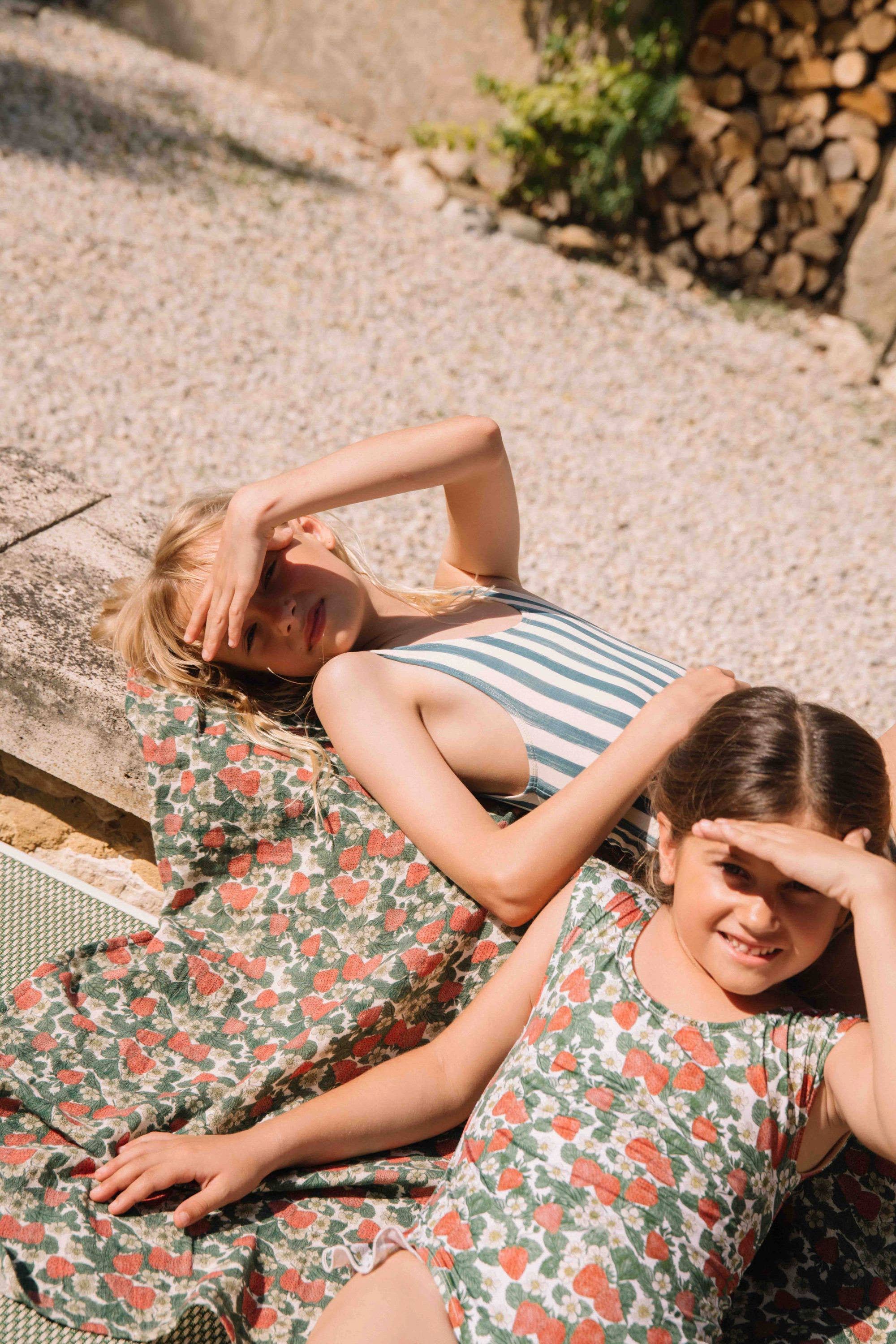 Two women in floral dresses lying on a stone surface with a rustic background.