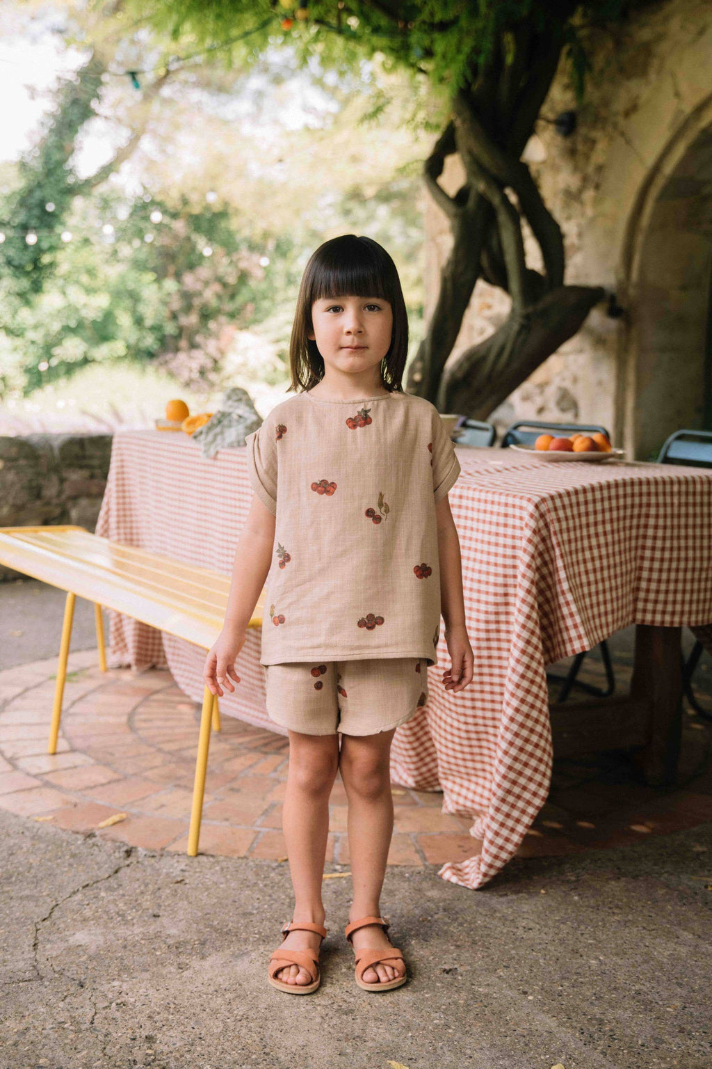 Young girl standing outdoors in front of a table with a checkered tablecloth.