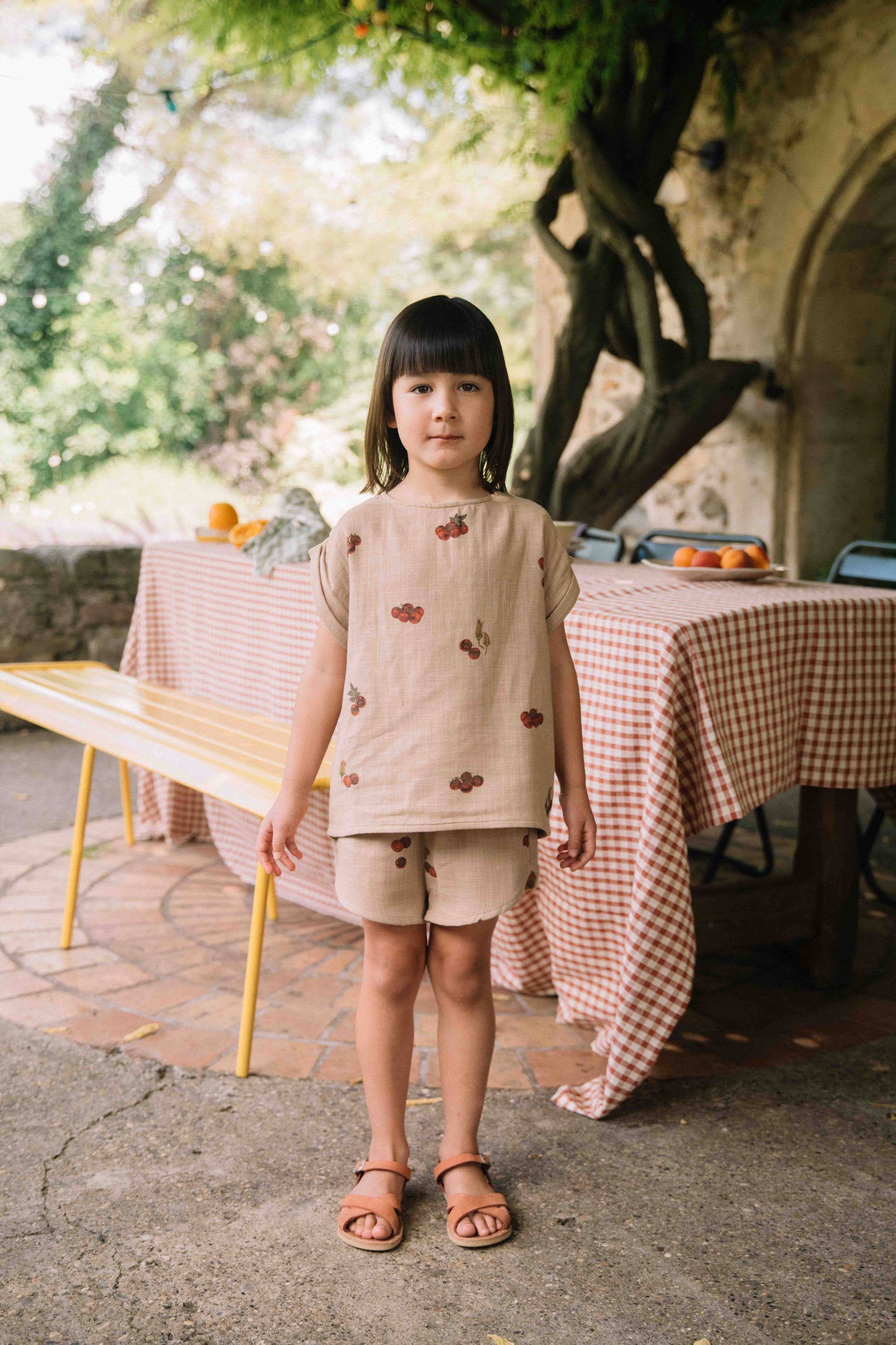 Young girl standing outdoors in front of a table with a checkered tablecloth.