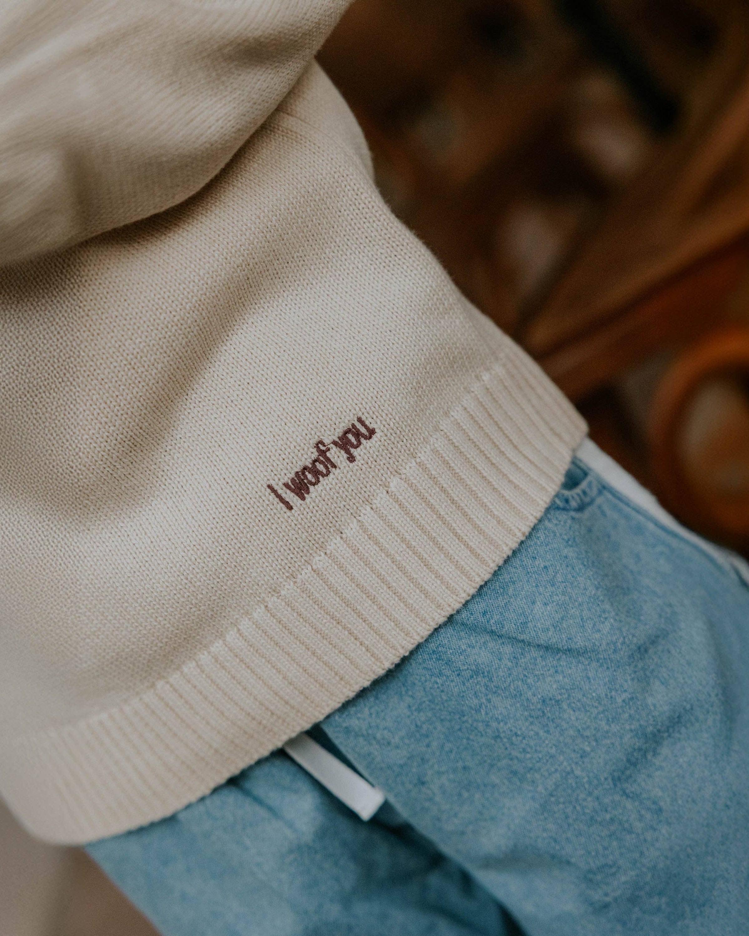 Close-up of a beige sweater with 'I woof you' embroidery on a blurred background