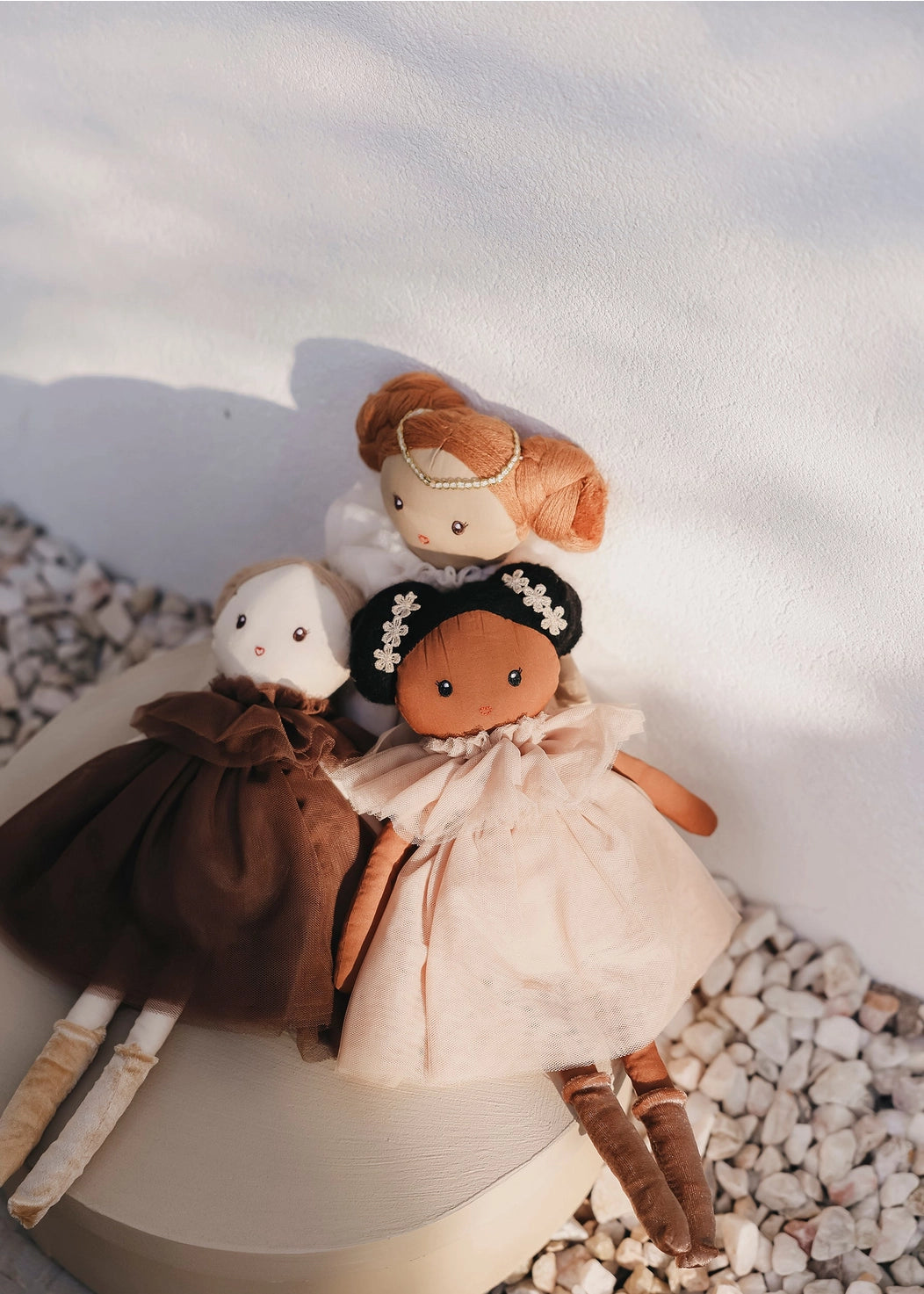 Three dolls with different hairstyles and outfits on a textured surface