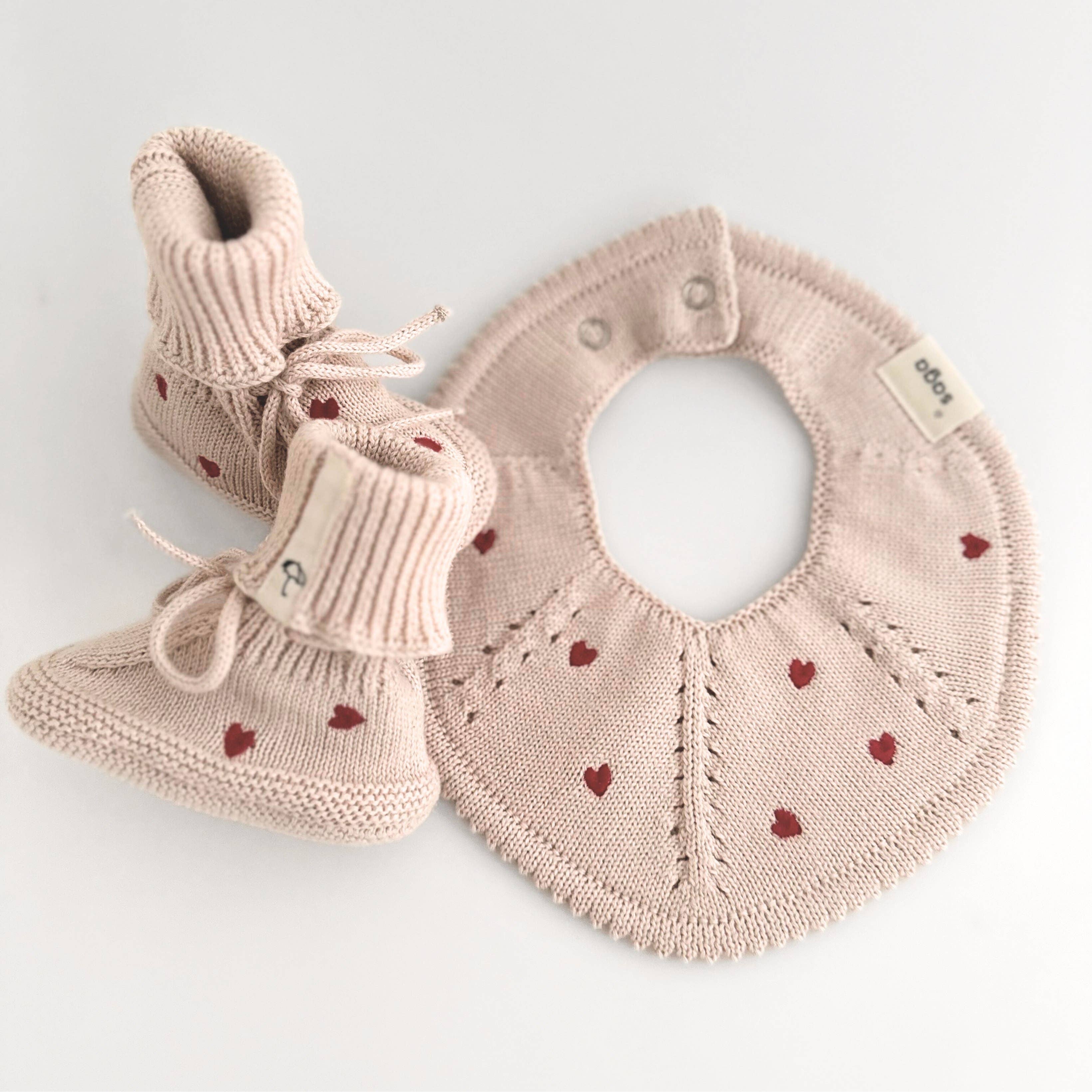 Baby booties and bib set with heart patterns on a light background