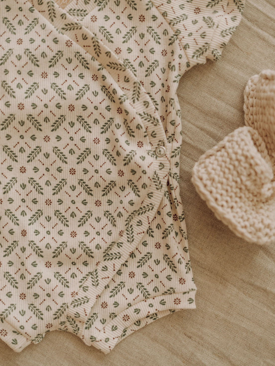 Baby romper with floral pattern and matching hat on a wooden surface