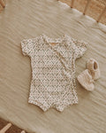 Baby romper with floral pattern and matching booties on a wooden surface