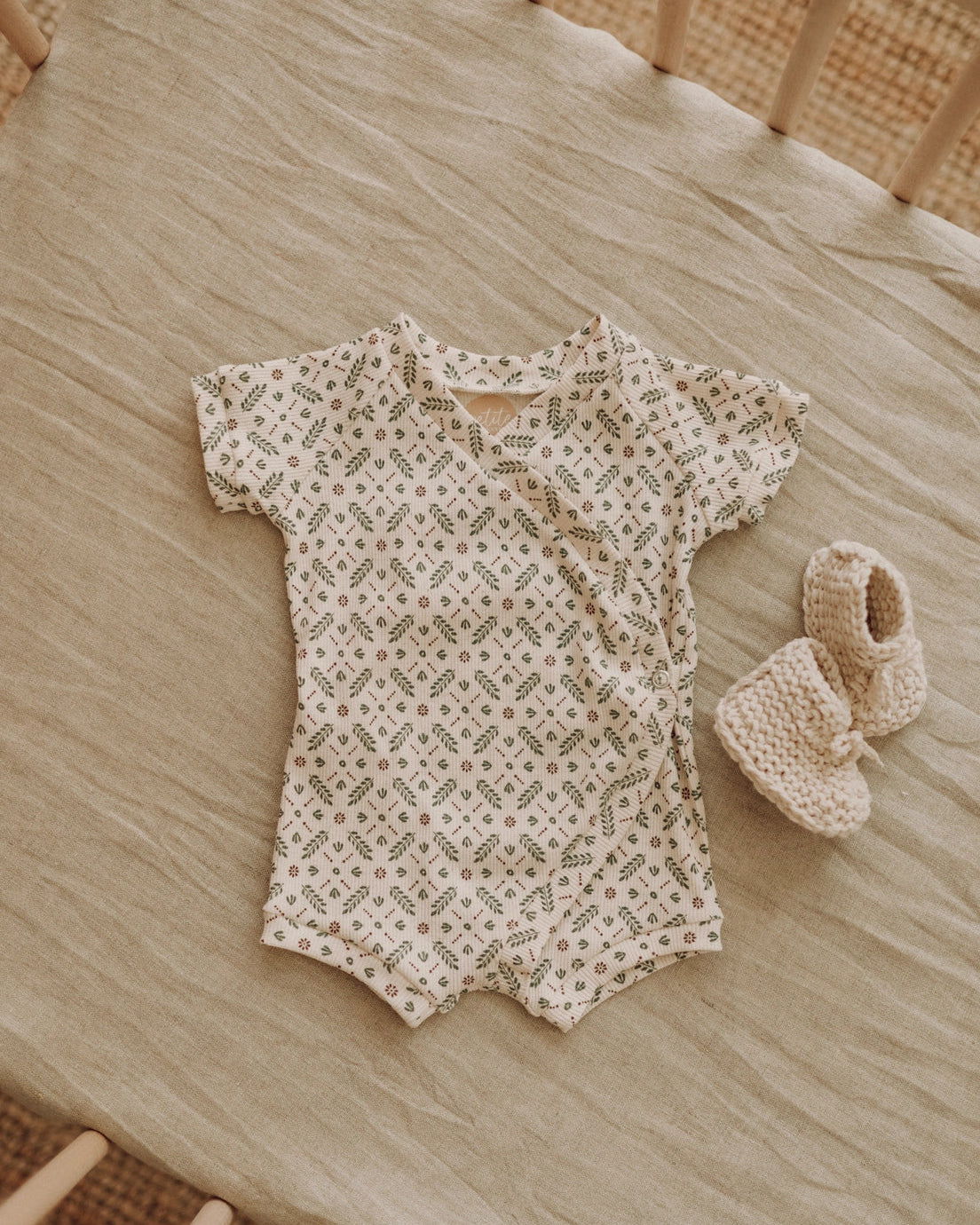 Baby romper with floral pattern and matching booties on a wooden surface