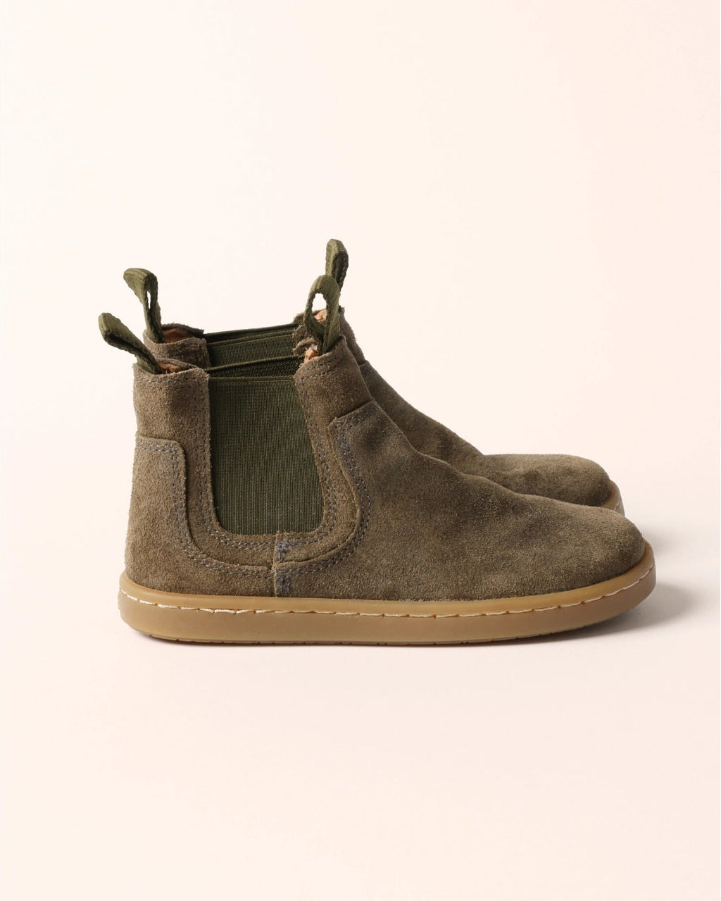 A pair of children's Chelsea-style ankle boots in brown suede with elastic side panels and pull tabs, shown on a light beige background.
