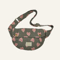 A quilted waist bag in olive green with a pink and red heart pattern, featuring a front flap with two gold snap buttons and an adjustable shoulder strap.