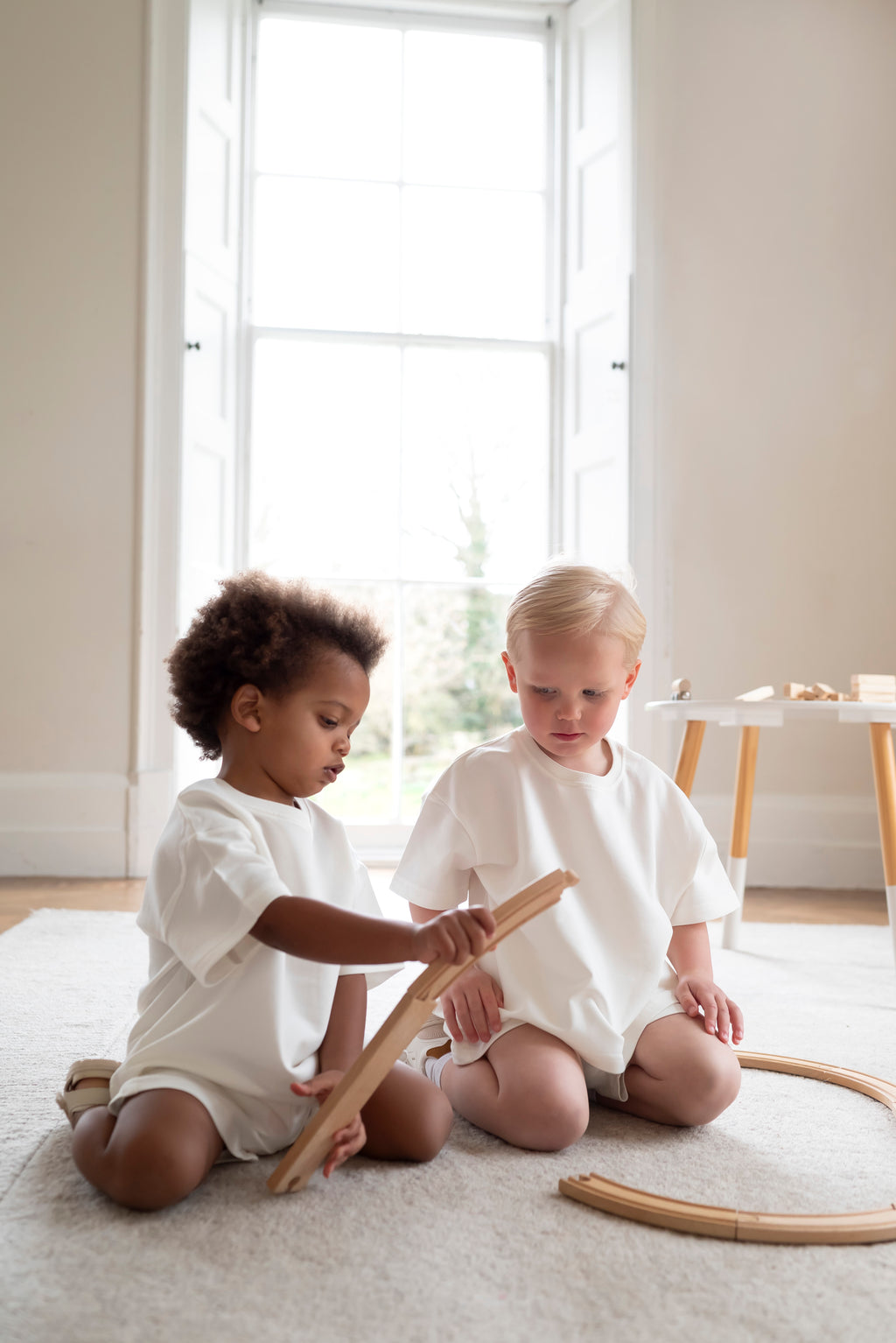 Two children playing with wooden toys on a light-colored rug.