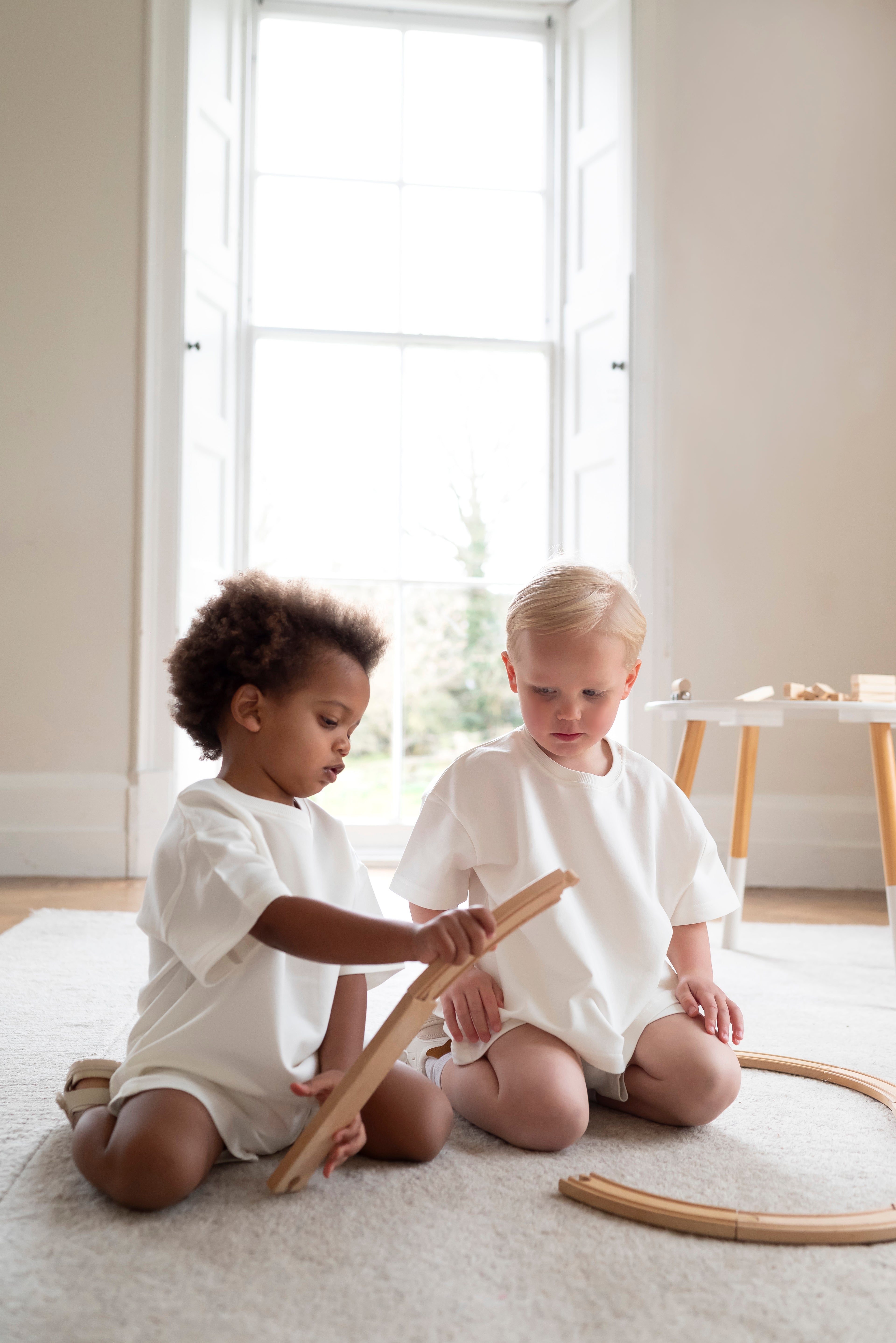 Two children playing with wooden toys on a light-colored rug.