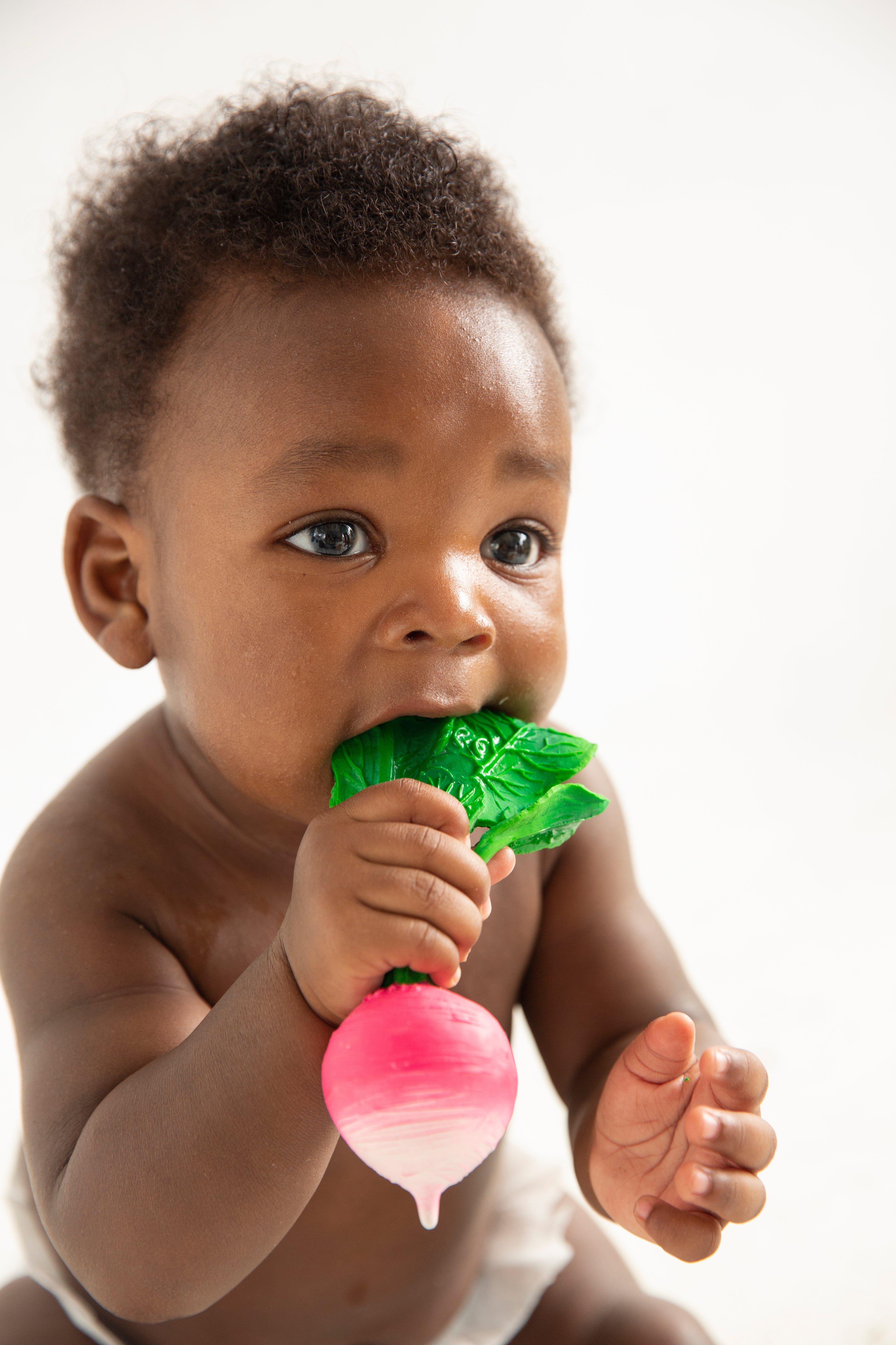 Baby holding a pink and green teething toy against a white background