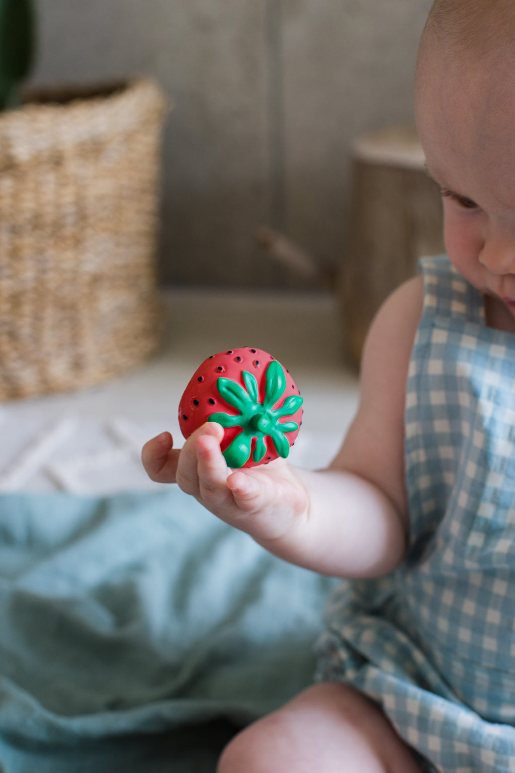 Child holding a red and green toy shaped like a strawberry.