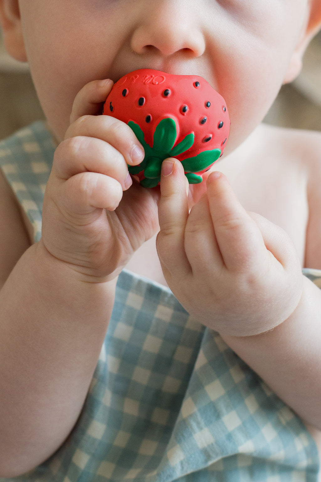 Baby holding a red strawberry-shaped teether