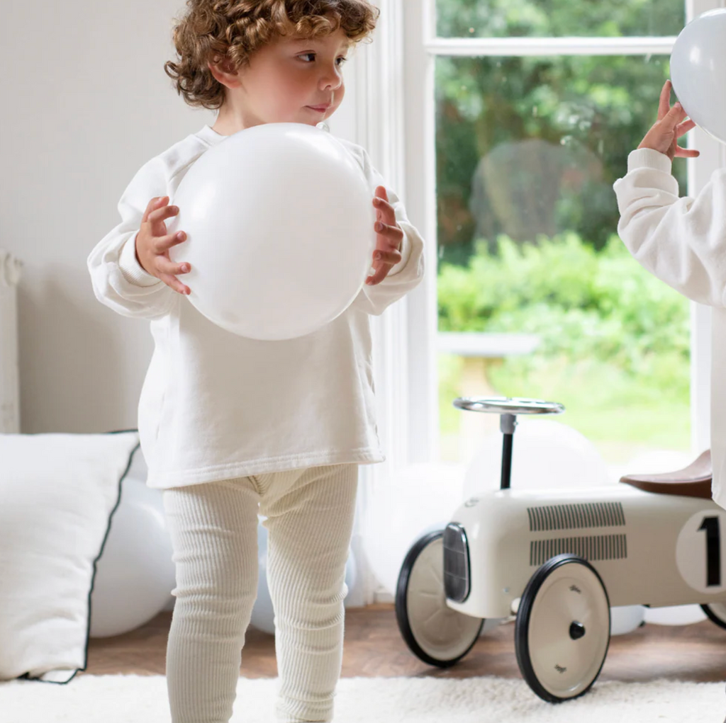 Child holding a white ball in a room with a toy car and a window in the background