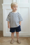 Child wearing a striped shirt and shorts standing indoors.