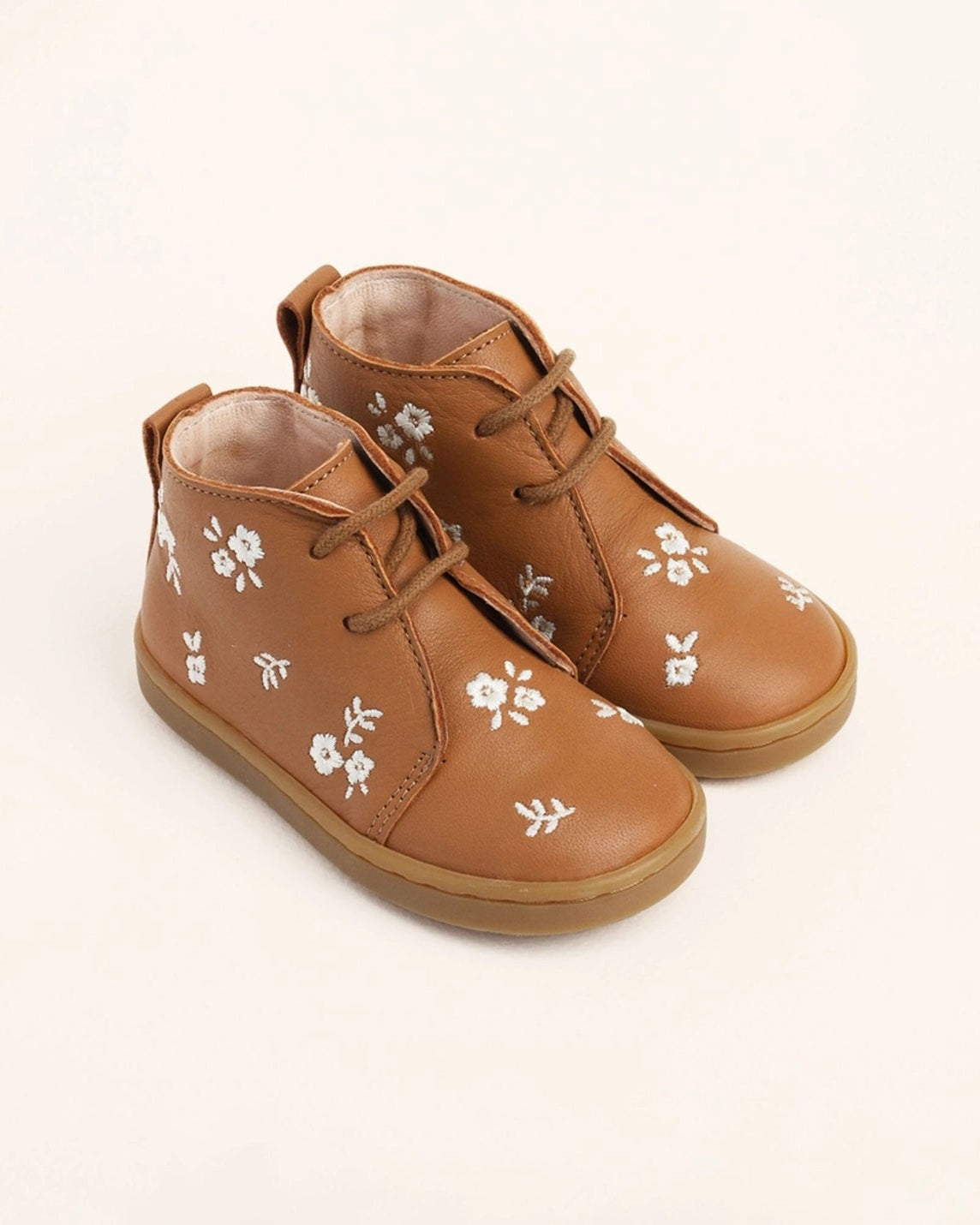 A pair of toddler's brown leather lace-up ankle boots decorated with small white floral patterns, shown on a clean off-white background.