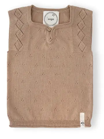 A sleeveless knit sweater vest in a warm taupe-beige color, featuring a henley-style collar with a button, textured knit body, and argyle diamond patterns on the shoulders. A circular white brand label reading 'saga' is visible inside the collar, and a small white tag is on the lower right hem.