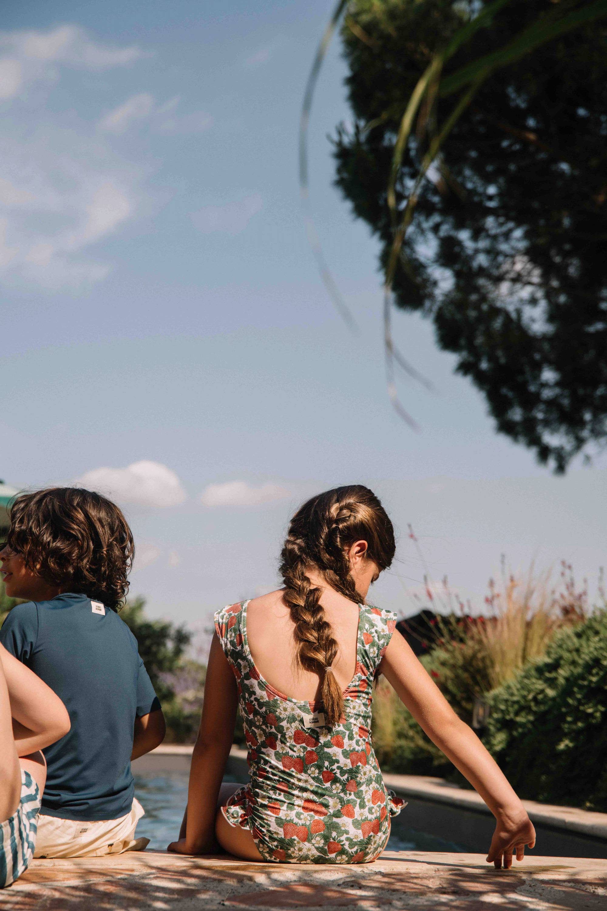 Two children by a pool with a clear sky and trees in the background