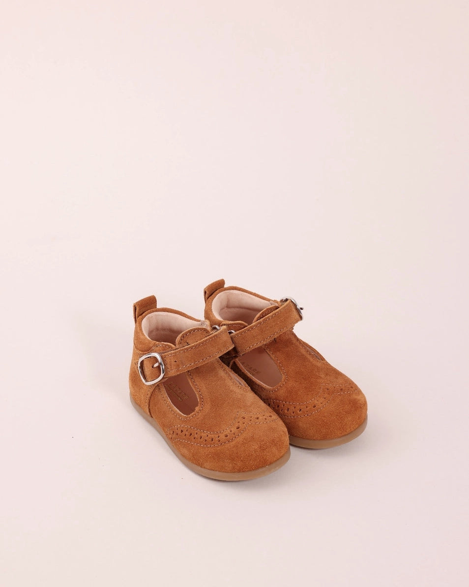 A pair of toddler Mary Jane shoes in light brown suede with silver buckle straps, shown on a plain light beige background.