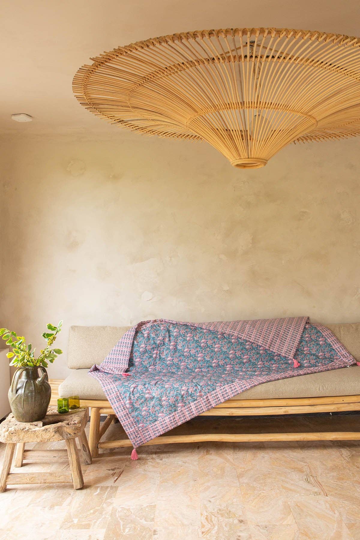 Woven ceiling light fixture above a bench with a floral blanket in a room with a textured wall.