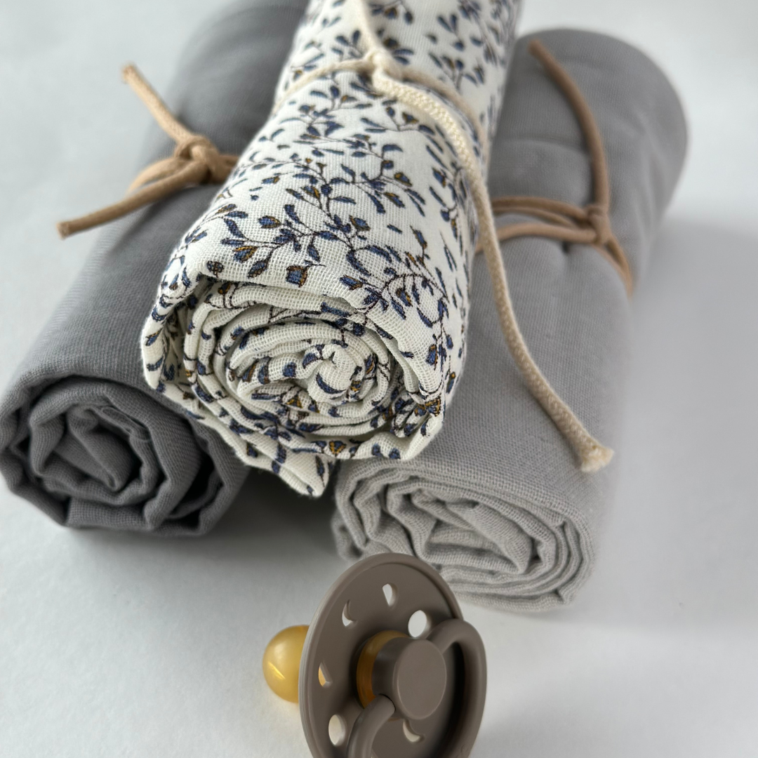 Rolled-up fabric with floral pattern and gray fabric, accompanied by a baby pacifier on a light background.