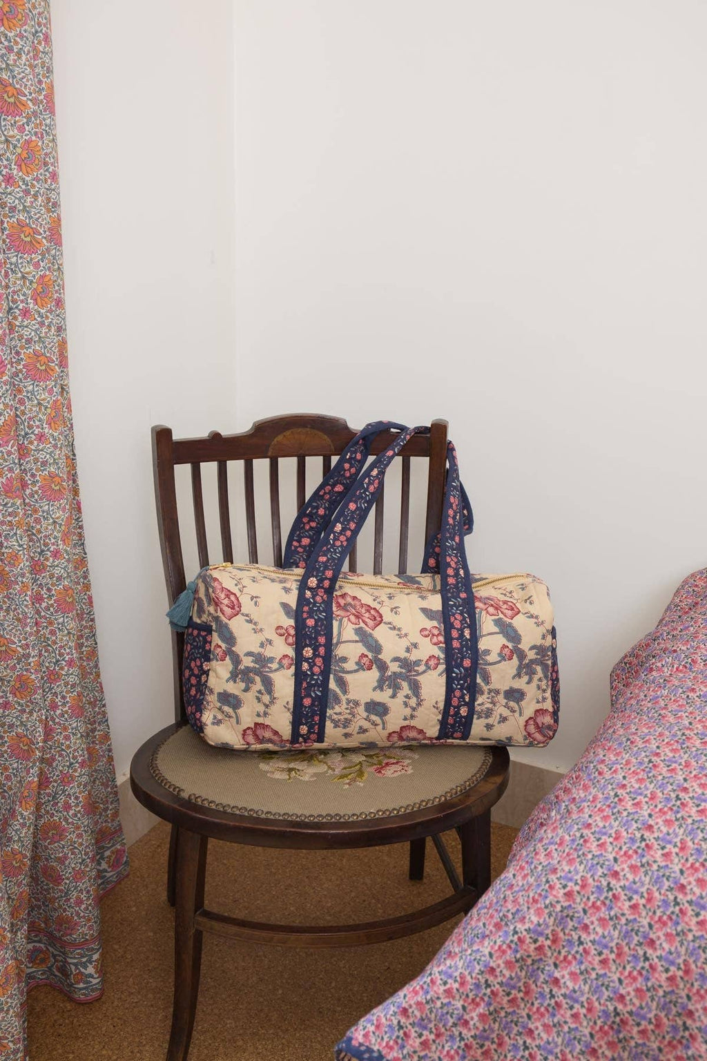 Floral-patterned bag on a wooden chair next to a bed with floral bedding.