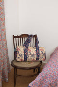 Floral-patterned bag on a wooden chair next to a bed with floral bedding.