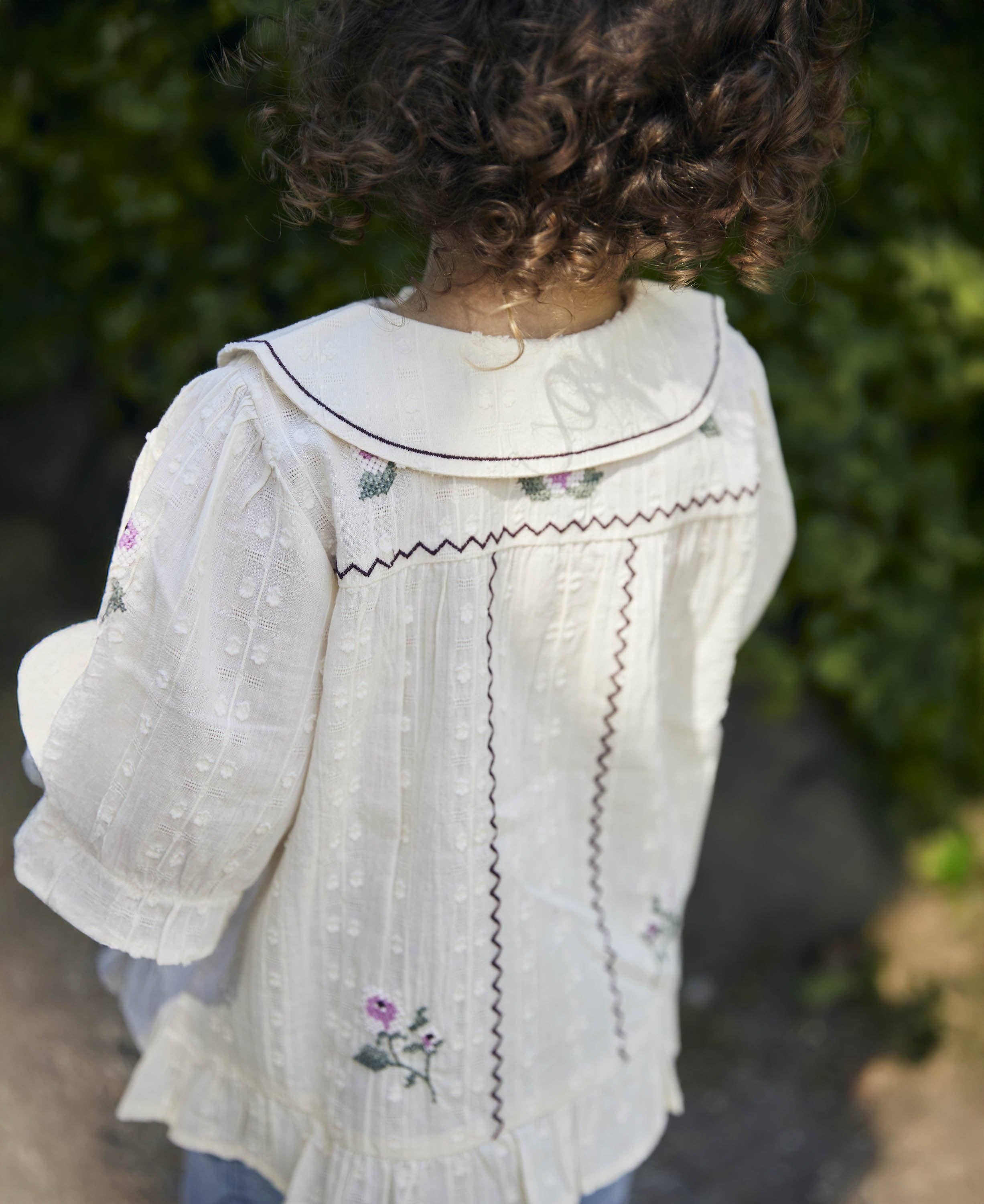 Child wearing a white embroidered blouse with a blurred green background