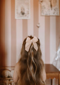Person with long hair wearing a decorative bow, standing in a room with striped wallpaper.