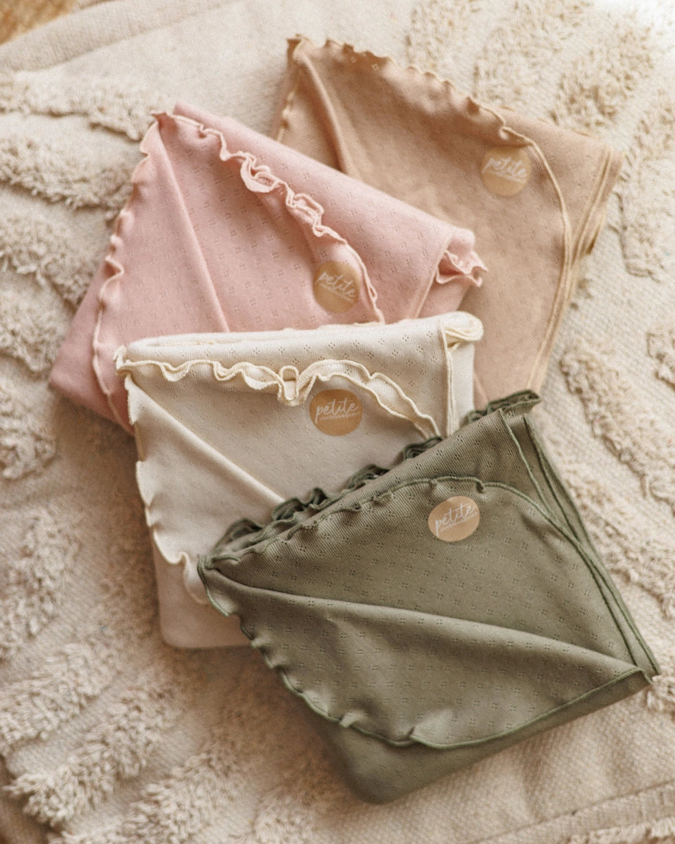 Four folded fabric items in pink, beige, white, and green on a textured surface.