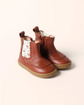 A pair of toddler brown leather ankle boots with a floral patterned elastic side panel and a tan sole, shown on a light beige background.