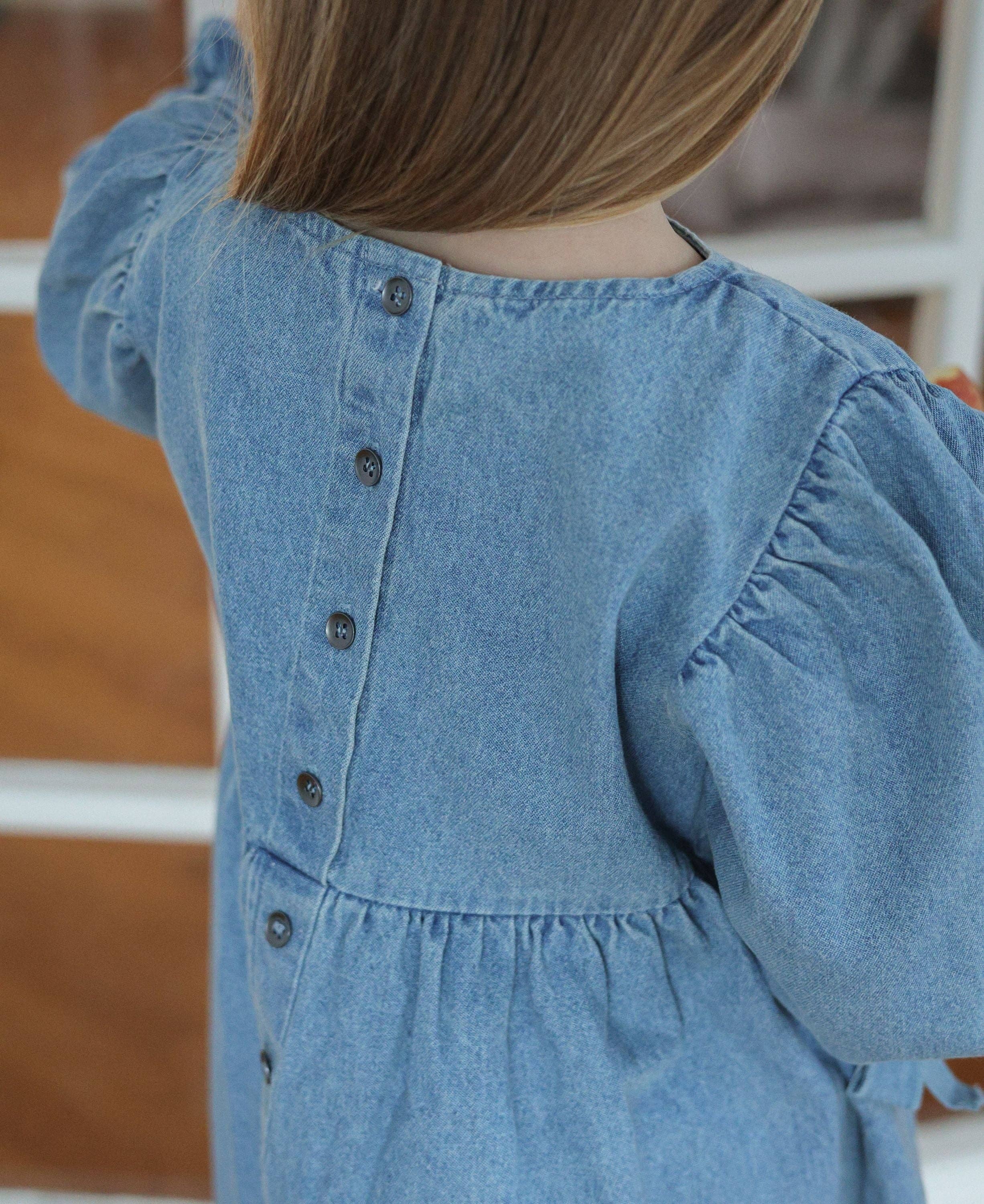 Close-up of a child wearing a blue denim dress with buttons.